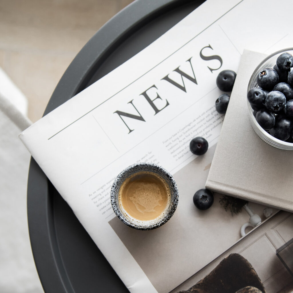 A newspaper with a cup of coffee and some blueberries.