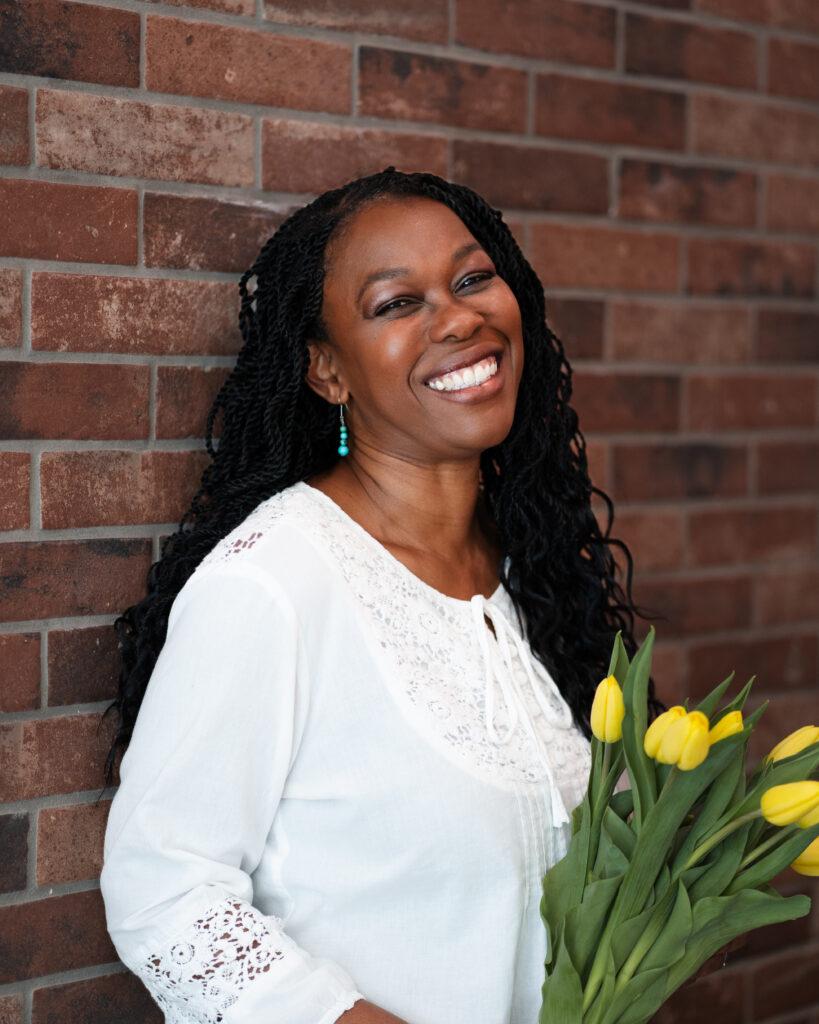 Laughing Black woman holds yellow tulips in front of a brick wall